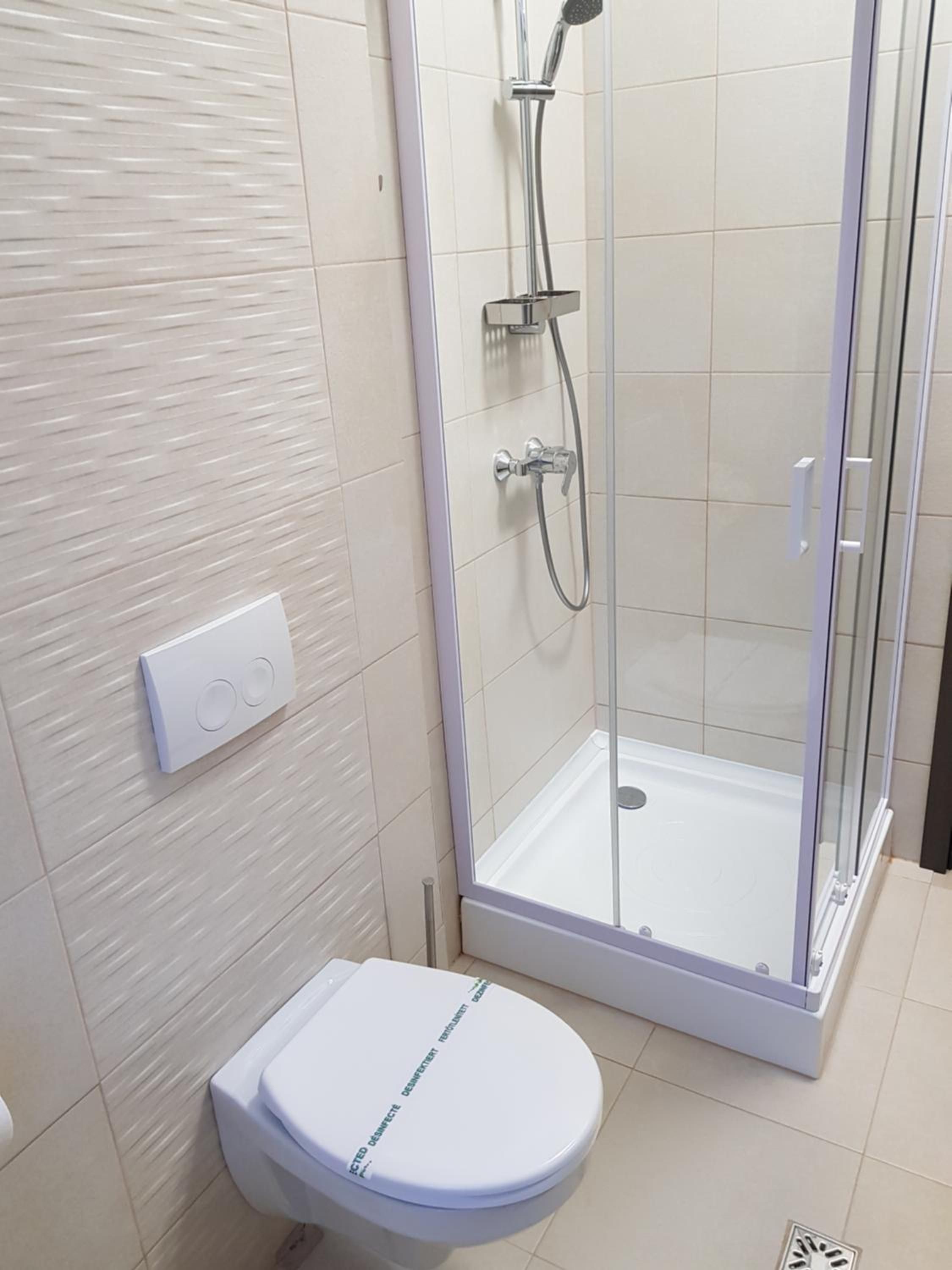 Une salle de bain comprenant des toilettes, une douche avec une porte en verre et un interrupteur fixé au mur.