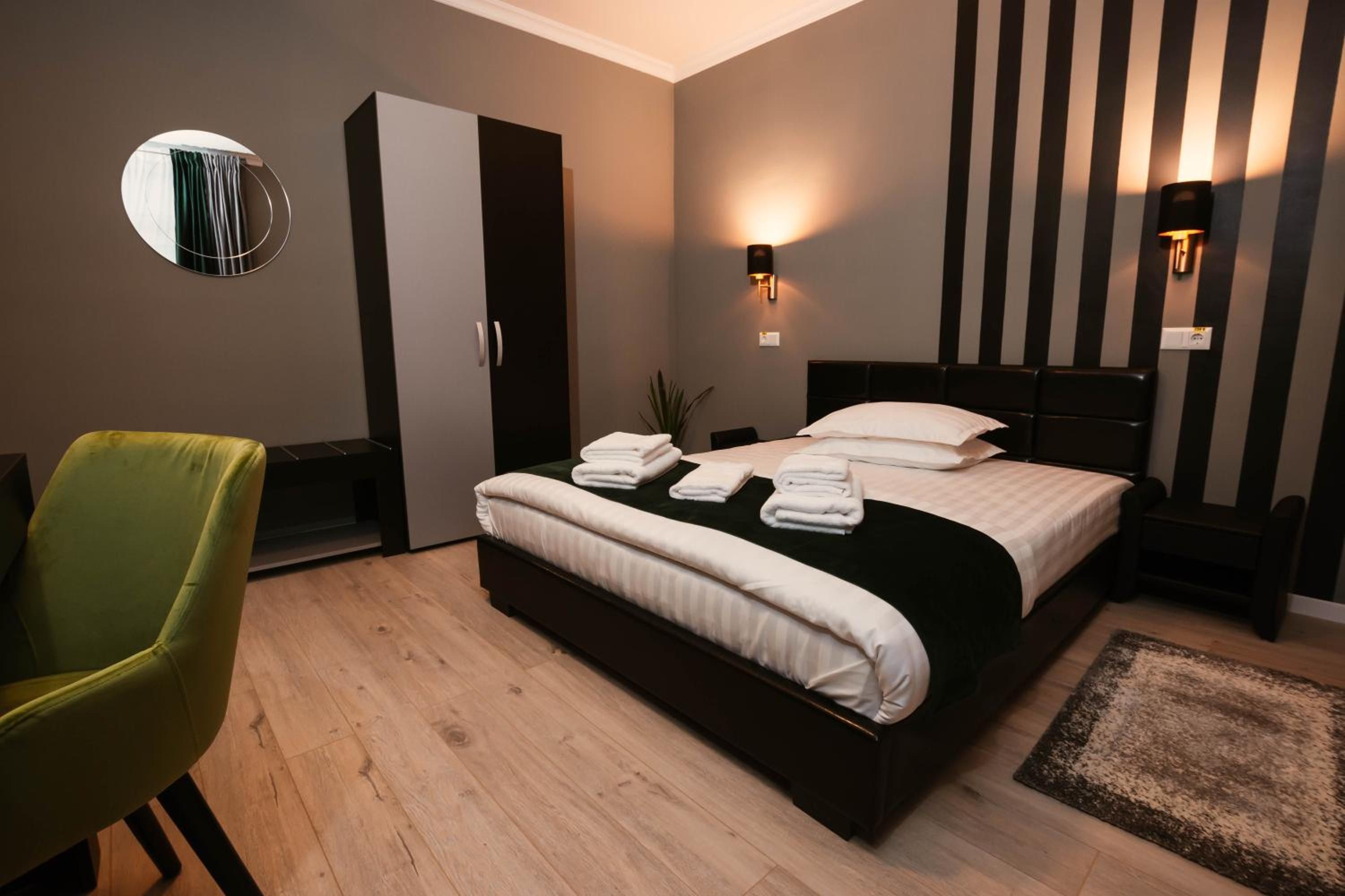 Hotellihuone, jossa on sänky, vihreä tuoli, vaatekaappi ja peili.