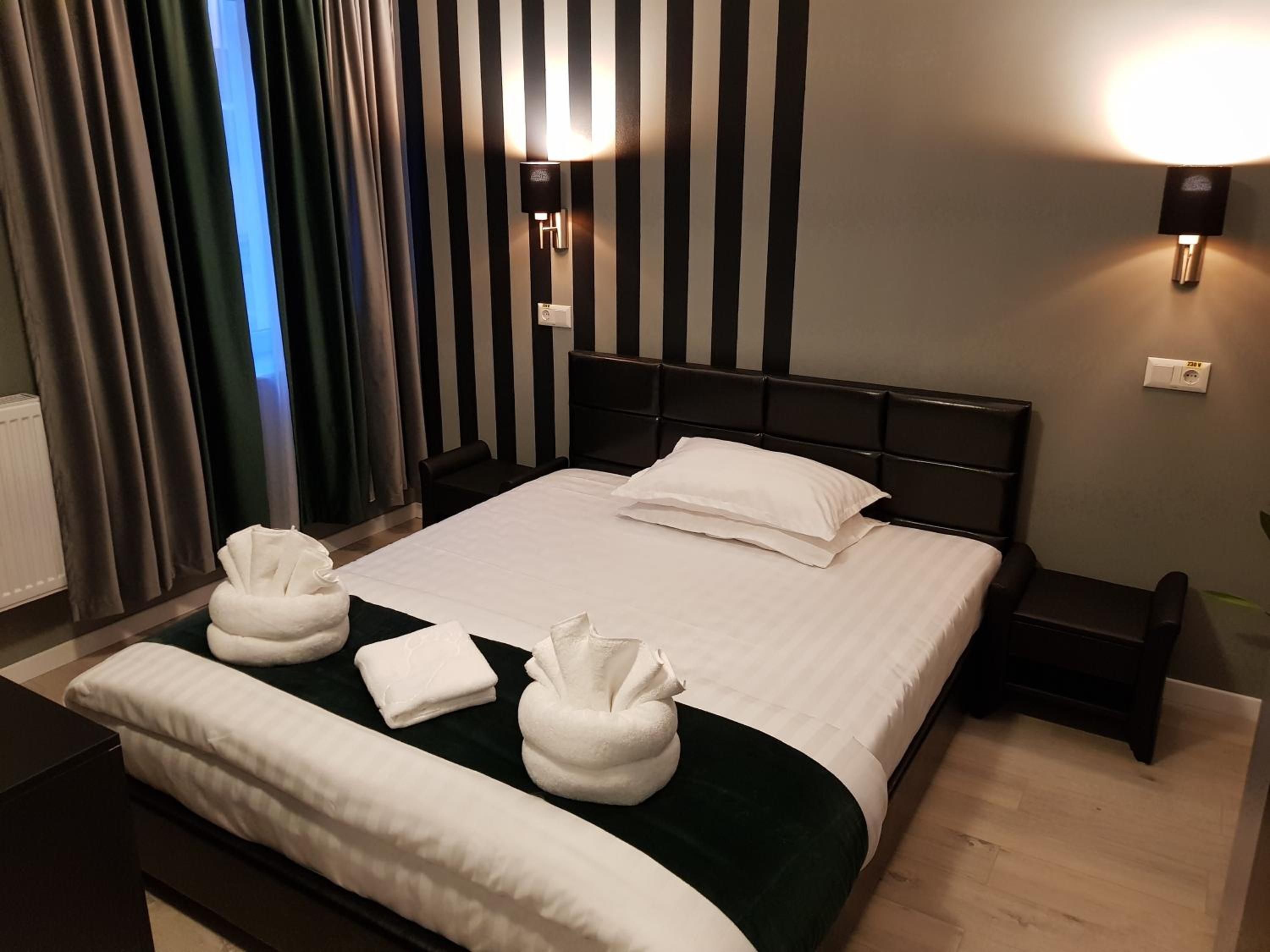 A hotel room with a large bed, two bedside tables, a headboard, and a window with curtains.