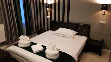 A hotel room with a large bed, two bedside tables, a headboard, and a window with curtains.