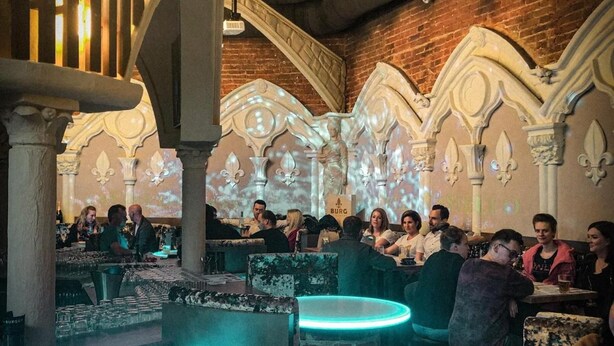 A restaurant with stone arches, a bar area with illuminated stools, and patrons seated at tables. - Burg Rooms 24h Self Check In (Spielberg)