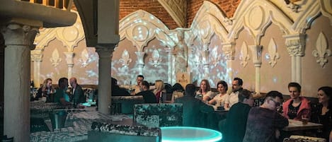 Un restaurante con arcos de piedra, una zona de bar con taburetes iluminados y clientes sentados en mesas.