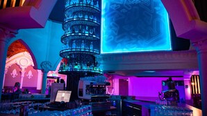 A bar area with a central column of bottles, a neon sign, and bar equipment. - Burg Rooms 24h Self Check In (Spielberg)
