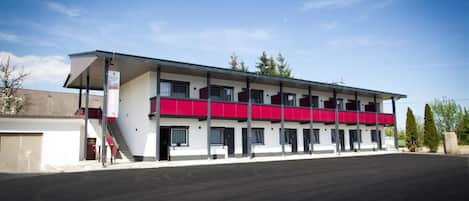 A two-story motel with a flat roof, a covered parking area, and a clear sky.