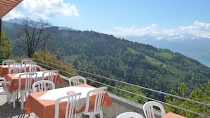 Una terraza al aire libre con mesas y sillas, con vistas a un paisaje montañoso y cielo despejado.