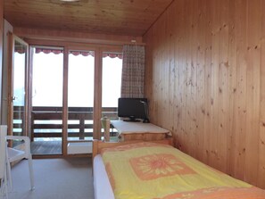 A room with a bed, a television on a table, a chair, and a sliding glass door leading to an outdoor area. - Hotel Bellevue (Heiligenschwendi)