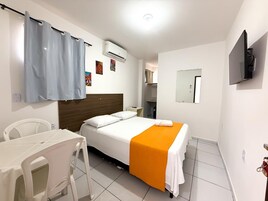 Habitación de hotel con cama, escritorio, silla, equipo de aire acondicionado, televisor y espejo.