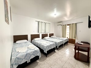 Quarto de hotel com três camas, uma pequena escrivaninha e uma televisão.