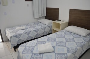 Habitación de hotel con dos camas, cada una con ropa de cama y almohadas estampadas, una mesita de noche con un control remoto y un interruptor de luz en la pared.