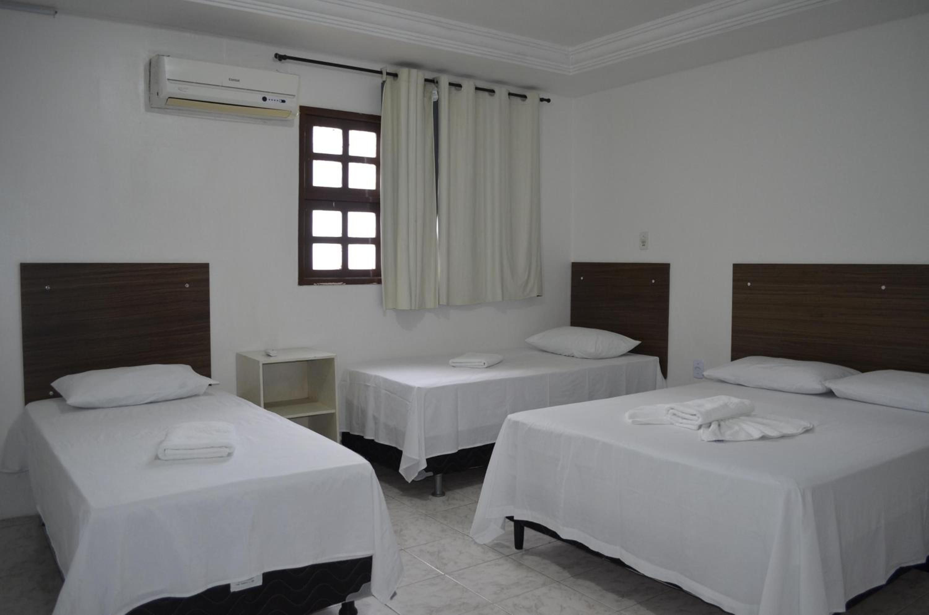 Quarto de hotel com duas camas de solteiro, uma pequena mesa de cabeceira e uma janela com cortinas.