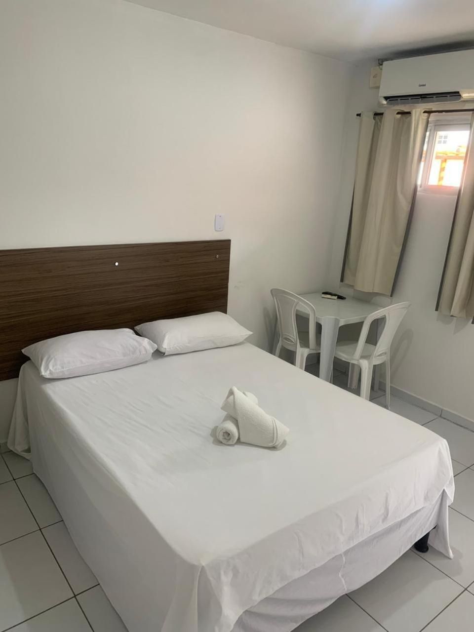 Quarto de hotel com cama, mesa pequena, cadeiras e aparelho de ar condicionado.