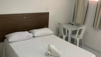 Quarto de hotel com cama, mesa pequena, cadeiras e aparelho de ar condicionado.