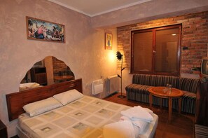 A hotel room with a bed, a sofa, a small table, a radiator, a window with blinds, and a painting on the wall. - Snow Heaven Hotel (Sofia)