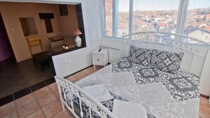 Un dormitorio con cama, mesita de noche, lámpara y vistas a la ciudad desde la ventana.