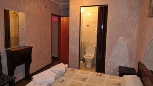 Habitación de hotel con cama, mesita de noche, espejo y baño visible a través de una puerta abierta.