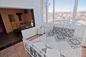 A bedroom with a bed, bedside table, lamp, and a view of the city through a window. - Snow Heaven Hotel (Sofia)