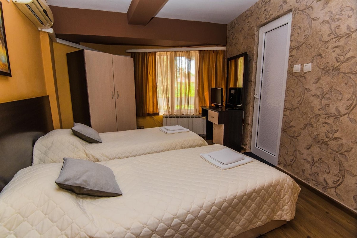 A hotel room with two beds, a wardrobe, a desk with a computer, and a window with curtains.