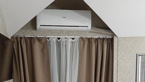 Una habitación con techo inclinado, unidad de aire acondicionado integrada, un banco, una mesa con papeles y una cortina.
