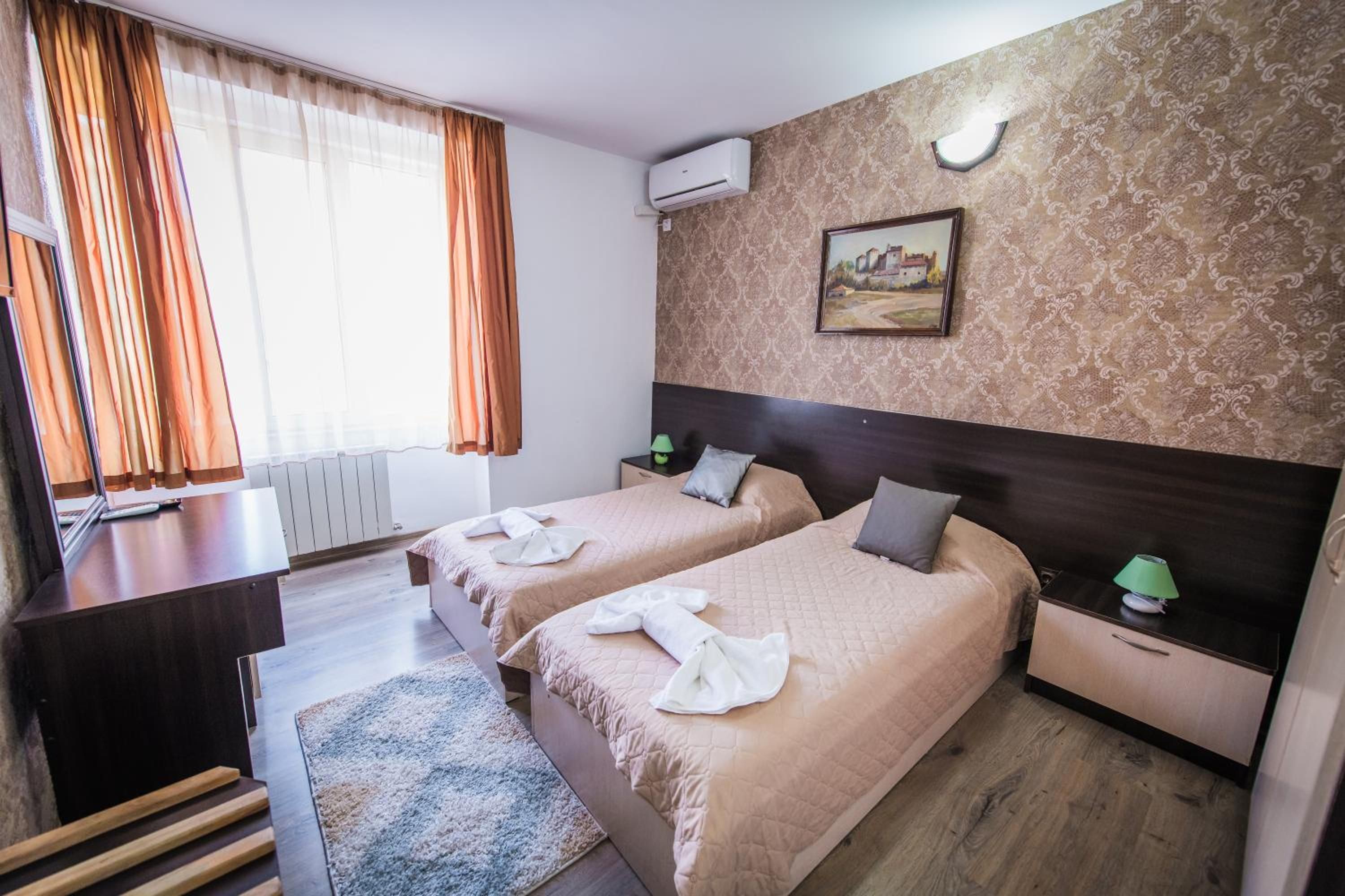 Habitación de hotel con dos camas, un escritorio, una silla, un radiador, un cuadro y una ventana con cortinas.