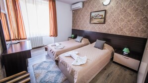Habitación de hotel con dos camas, un escritorio, una silla, un radiador, un cuadro y una ventana con cortinas.