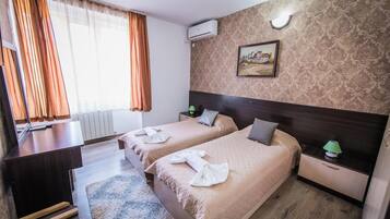 Habitación de hotel con dos camas, un escritorio, una silla, un radiador, un cuadro y una ventana con cortinas.