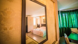Habitación de hotel con una cama, un escritorio y una silla. Hay un espejo en la pared y una ventana con cortinas.