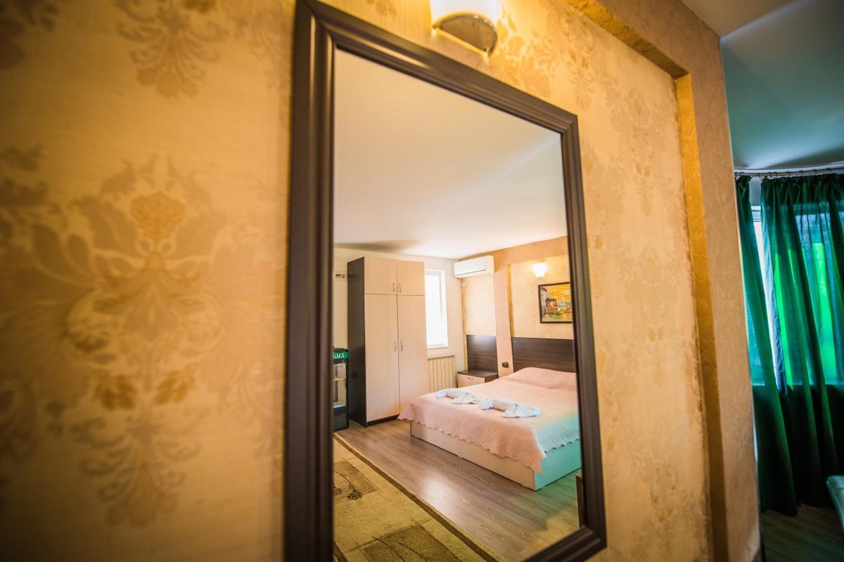 Una habitación de hotel con un espejo grande, una cama, una mesita de noche, un armario y un cuadro en la pared.