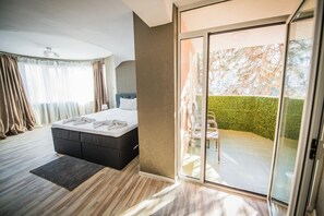 Un dormitorio moderno con una cama grande, una puerta corrediza de vidrio a un balcón y vistas de un seto.