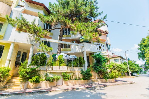 A multi-story hotel with balconies, outdoor seating, and lush greenery.