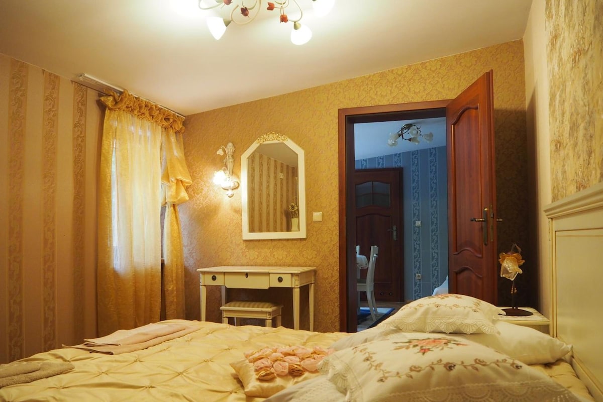 Un dormitorio con cama, mesita de noche, espejo, puerta y cortinas.