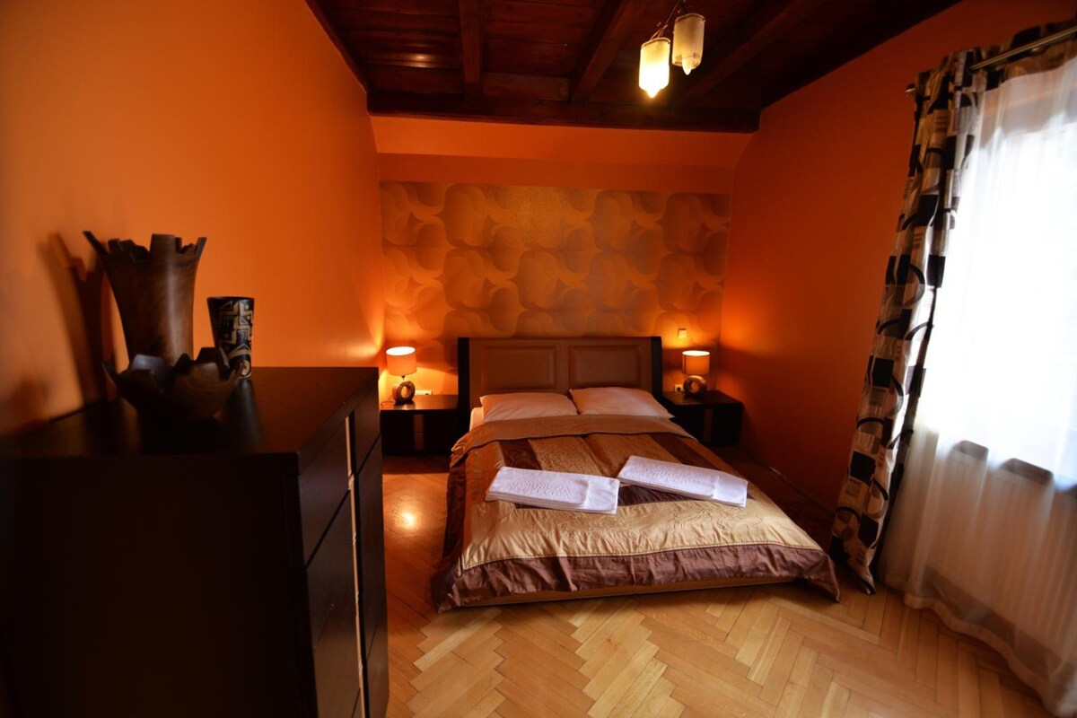 Una habitación de hotel con techo de madera, una cama con cubrecama marrón, dos lámparas de noche y una mesita de noche de madera.
