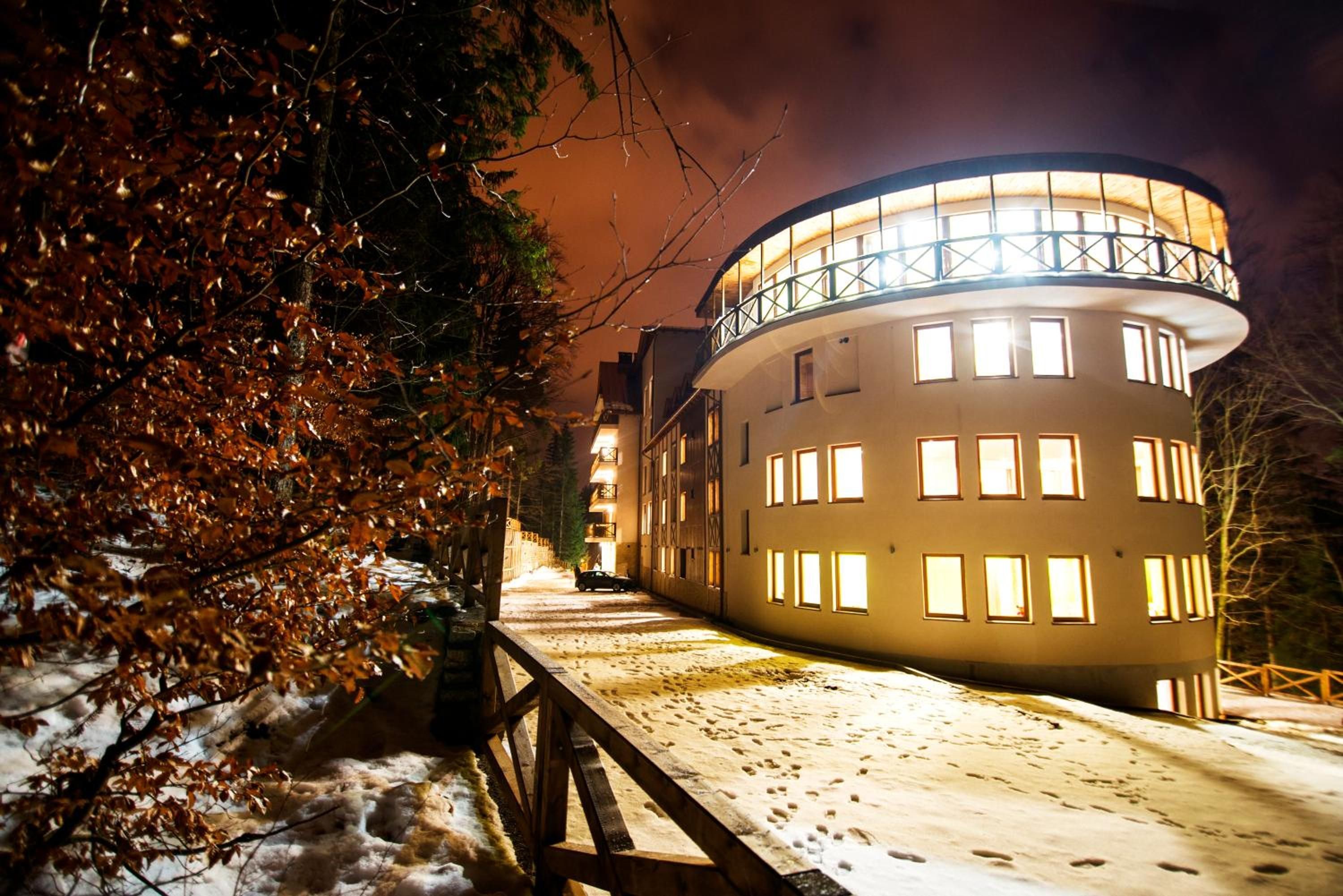 Un edificio con estructura circular y varias ventanas, rodeado de árboles y un sendero cubierto de nieve.