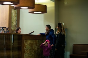 Un área de recepción con un mostrador de madera, un separador de vidrio y un teléfono instalado en la pared.