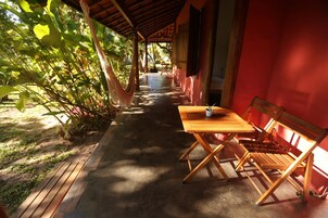 Un espacio de estar al aire libre cubierto con una mesa y bancos, rodeado de vegetación.