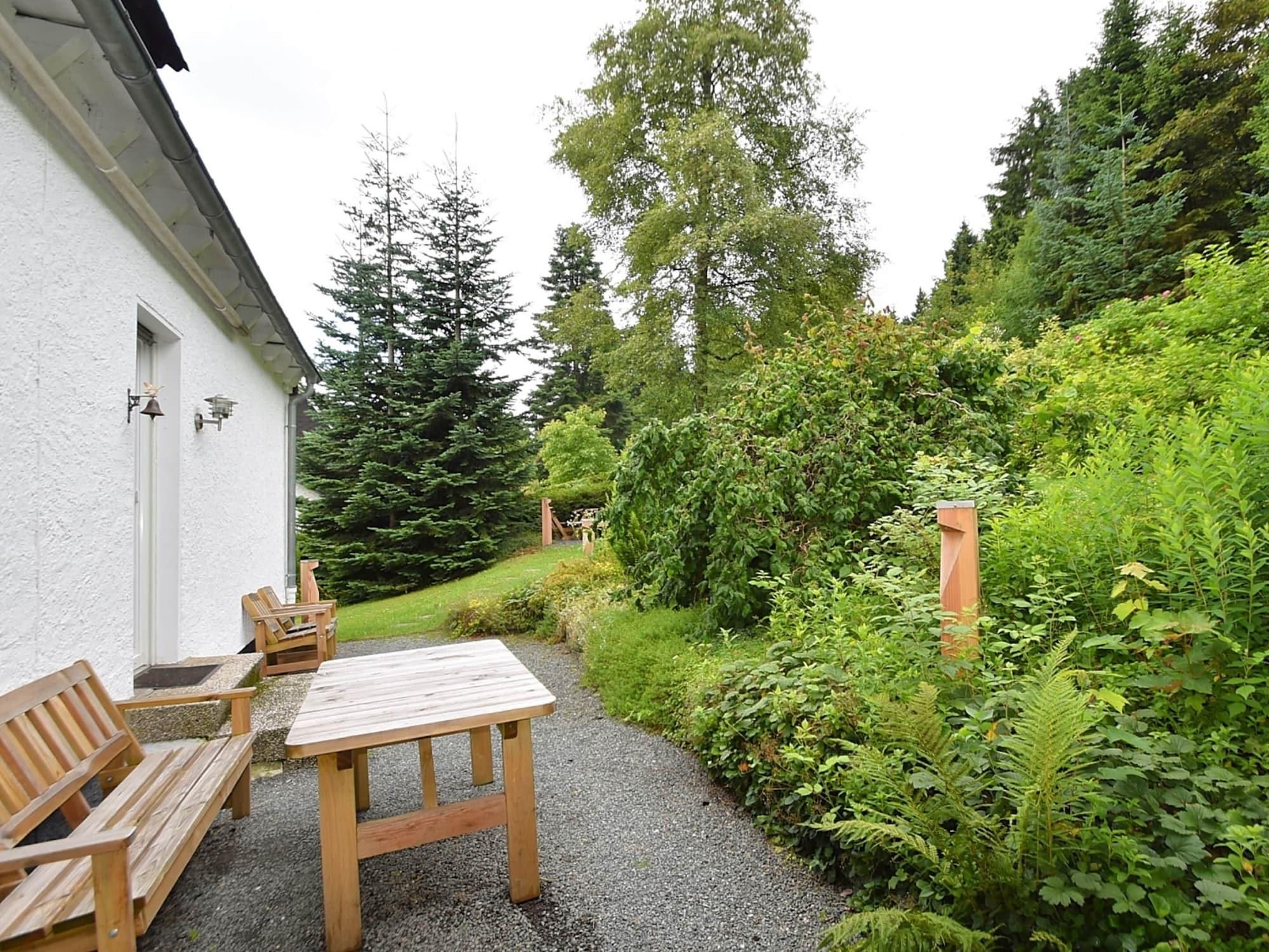 Un patio con una mesa y sillas de madera, rodeado de abundante follaje y árboles.