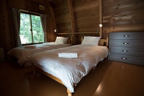 A wooden cabin bedroom with two beds, a dresser, and a window with curtains. - Yukiita Lodge (Hakuba)