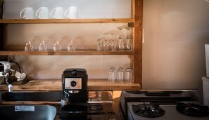A kitchen with a coffee maker, a stove, and shelves with cups and glasses. - Yukiita Lodge (Hakuba)