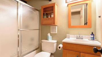 A bathroom with a toilet, a sink, a mirror, and a cabinet.