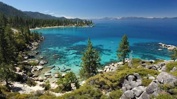 A coastal landscape with clear turquoise waters, rocky shores, and dense forested areas.