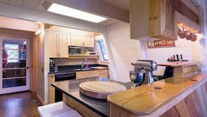 A compact kitchen with wooden cabinets, a microwave, a sink, a wooden countertop, and a hanging pot rack. - Zephyr By Avantstay Stylish Modified A Frame W/ (Truckee)