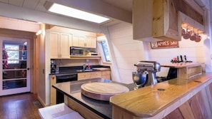 A compact kitchen with wooden cabinets, a microwave, a sink, a wooden countertop, and a hanging pot rack. - Zephyr By Avantstay Stylish Modified A Frame W/ (Truckee)