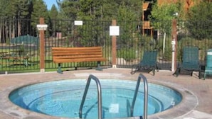 A swimming pool with a wooden bench and lounge chairs, surrounded by a fence and trees. - Zephyr By Avantstay Stylish Modified A Frame W/ (Truckee)