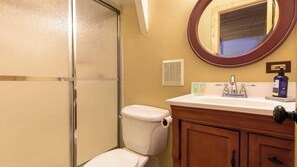 Baño con inodoro, lavamanos, espejo y mampara de ducha.