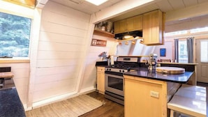 A compact kitchen with wooden cabinets, a stove, and a small island with a mixer. - Zephyr By Avantstay Stylish Modified A Frame W/ (Truckee)