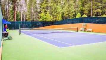 Cancha de tenis exterior con red, rodeada de césped y una valla.
