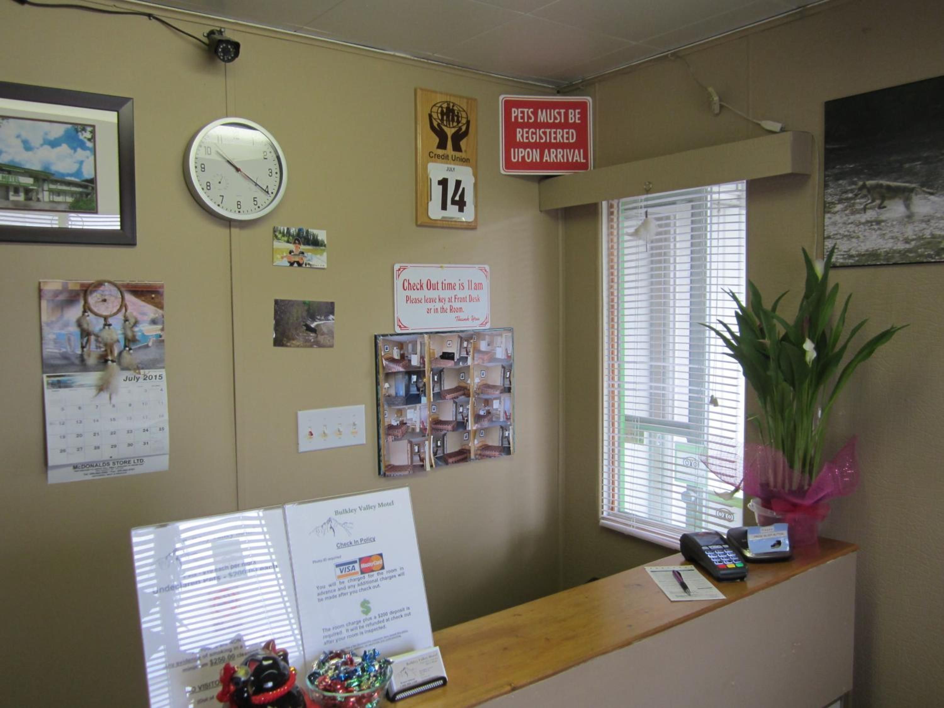 Una recepción con un reloj, un calendario, un cartel sobre registro de mascotas y una ventana con persianas.