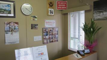 A reception desk with a clock, a calendar, a sign about pet registration, and a window with blinds.