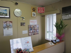 A reception desk with a clock, a calendar, a sign about pet registration, and a window with blinds.