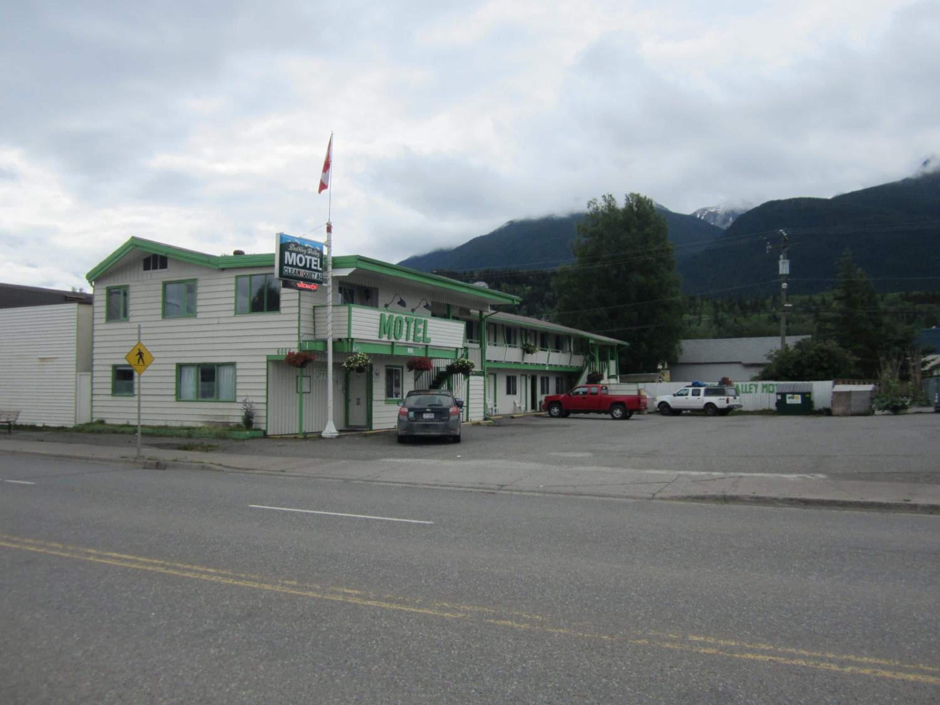 A motel with a green and white facade, a flag, and a pedestrian crossing sign.