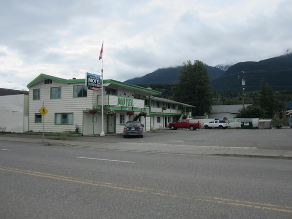 A motel with a green and white facade, a flag, and a pedestrian crossing sign.